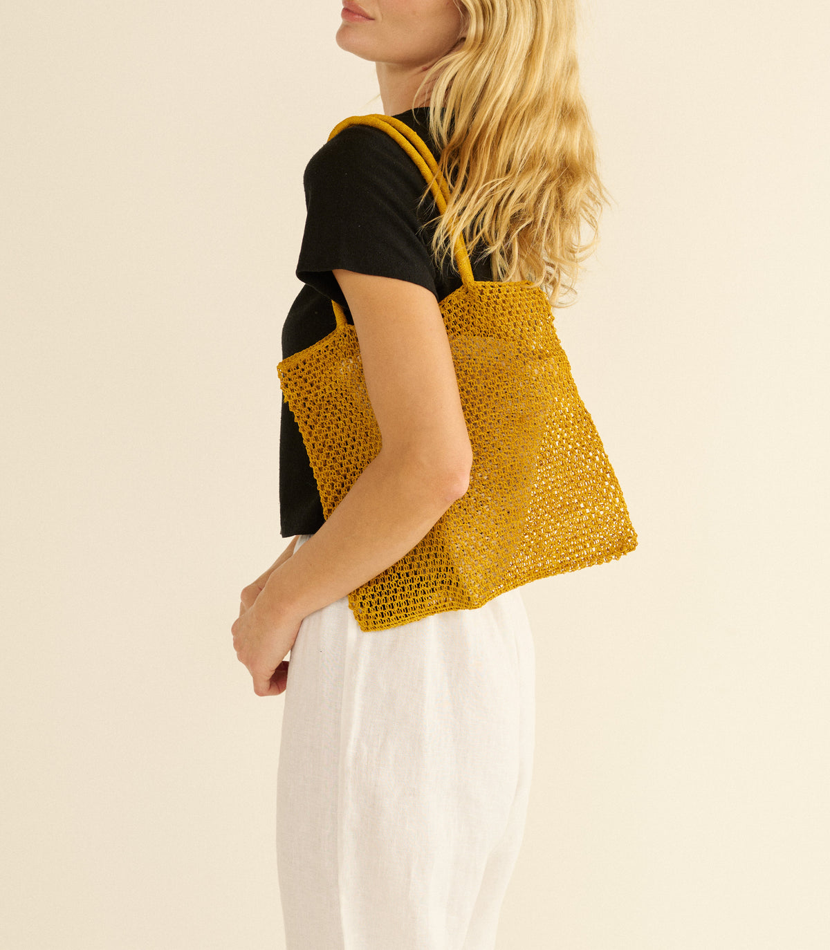 Woman holding a yellow knitted tote bag against a beige background