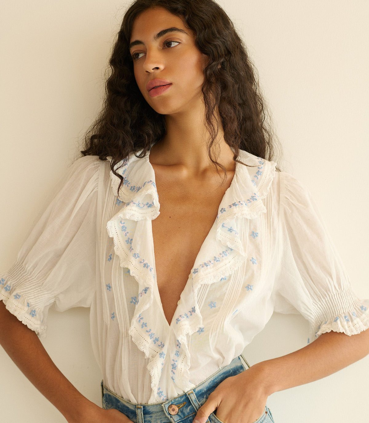 Woman wearing a white blouse with blue floral and blue jeans against a plain background